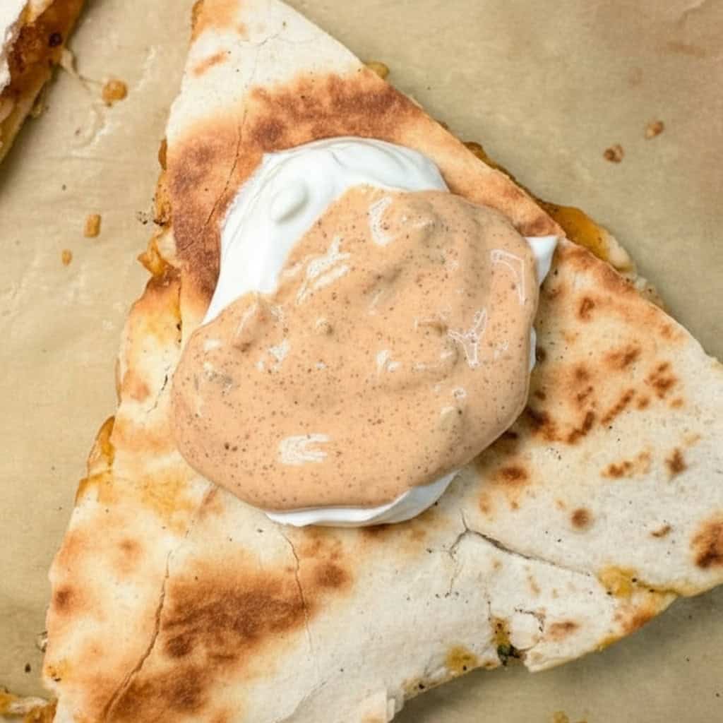 Savory quesadilla filled with melted cheese, topped with creamy spicy sauce, served on parchment paper for a delicious meal. Perfect for snack or lunch, easy to prepare with simple ingredients.