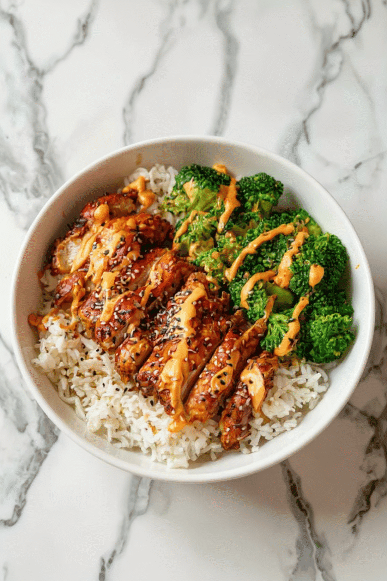 Sweet and savory Asian-inspired chicken rice bowl with broccoli, drizzled with spicy peanut sauce, topped with black sesame seeds on a marble background.