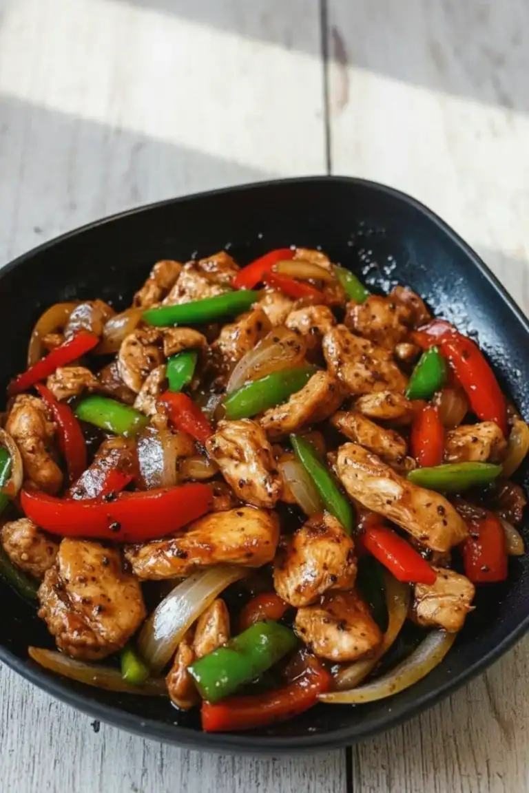 Stir-fried chicken with colorful bell peppers and onions in a black bowl, showcasing a flavorful Asian-inspired dish.